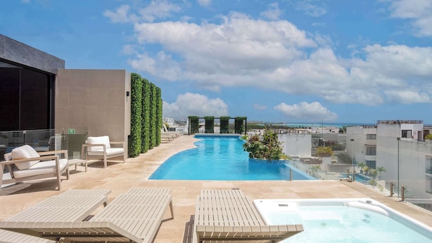 Una piscina en la azotea con sillones de descanso, un jacuzzi y vistas a la ciudad y al océano.