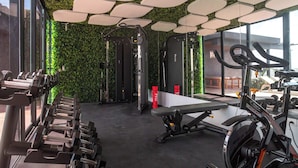 Un gimnasio con equipo de ejercicio, una banca y una pared cubierta de vegetación.
