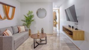 Una sala de estar moderna con un sofá gris, una mesa de centro redonda, una planta en maceta, un espejo y un televisor montado en la pared.