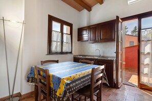 A kitchen with wooden cabinets, a dining table with a tablecloth, and a view to the outside.