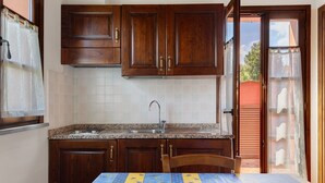 Uma cozinha com armários de madeira, bancada de granito, pia e mesa com toalha de mesa florida.
