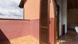 Uma varanda com porta de madeira, piso de azulejos e um quarto com cama e micro-ondas.