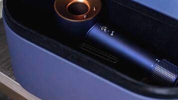 A blue, cylindrical object with a metallic ring and a small metallic component, possibly a speaker or device, on a surface with a tiled floor.