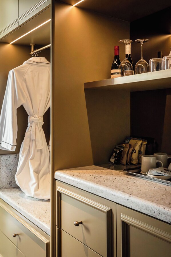 Une salle de bain avec un peignoir suspendu à un porte-serviettes, un plan de travail avec une machine à café et une étagère avec des bouteilles et des verres.