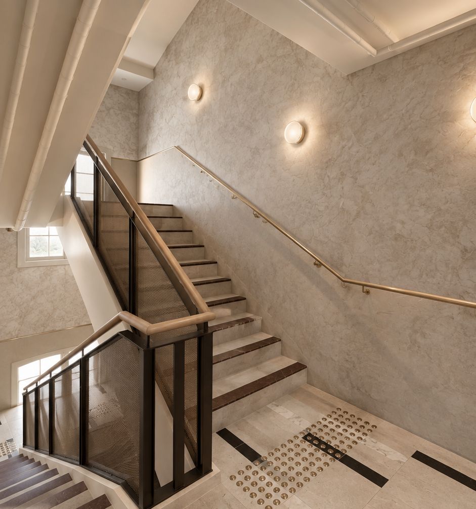 A modern staircase with a glass railing, a handrail, and a patterned floor.