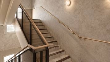 A modern staircase with a glass railing, a handrail, and a patterned floor.