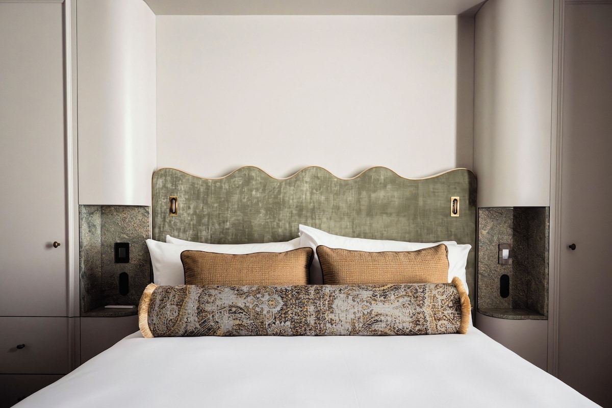 A neatly made bed with a patterned bedspread and two pillows, flanked by two bedside tables with lamps.