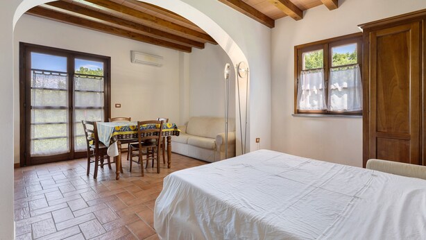 Une chambre à coucher avec un lit, une table à manger avec des chaises, un canapé et une fenêtre avec des rideaux.