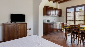 Une chambre comprenant un lit, un téléviseur et un coin cuisine avec des meubles en bois et un four à micro-ondes.