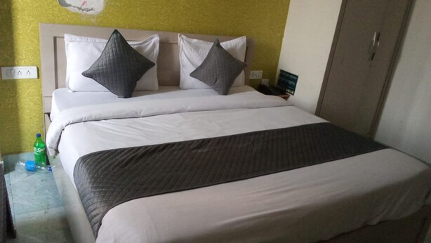 Ein Hotelzimmer mit einem Bett, zwei Kissen, einer Decke, einem Nachttisch mit einer Flasche und einem Kleiderschrank.