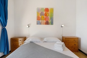 Quarto com cama, duas mesas de cabeceira, um quadro na parede e uma cortina azul.