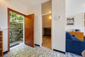 Quarto com porta de madeira que dá para uma parede de pedra, sofá azul, relógio e quadro na parede.