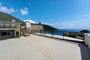 A rooftop terrace with a view of the sea, a stone wall, and a metal railing.