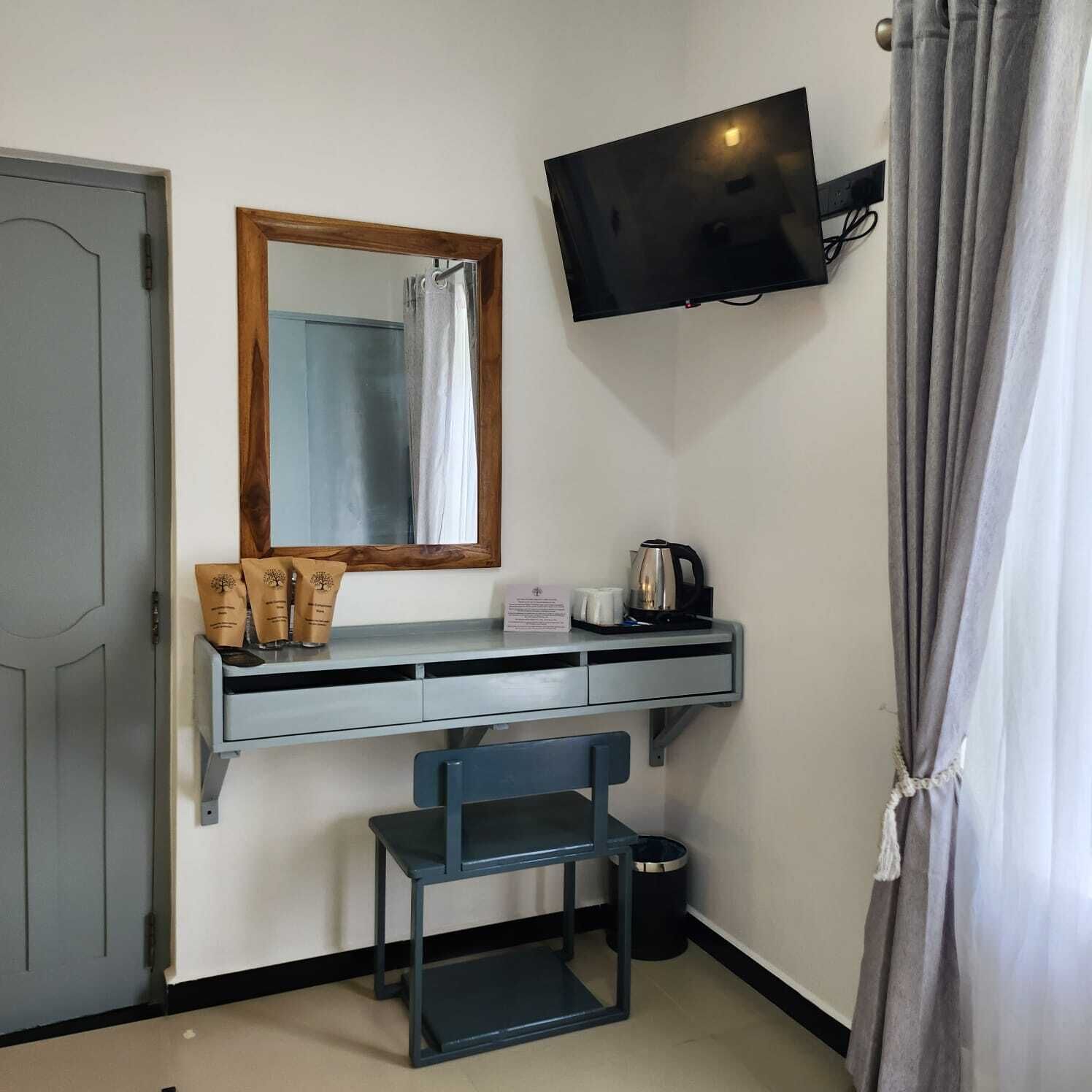 Een kleine kamer met een bureau, een stoel, een aan de muur bevestigde televisie en een kleine prullenbak.