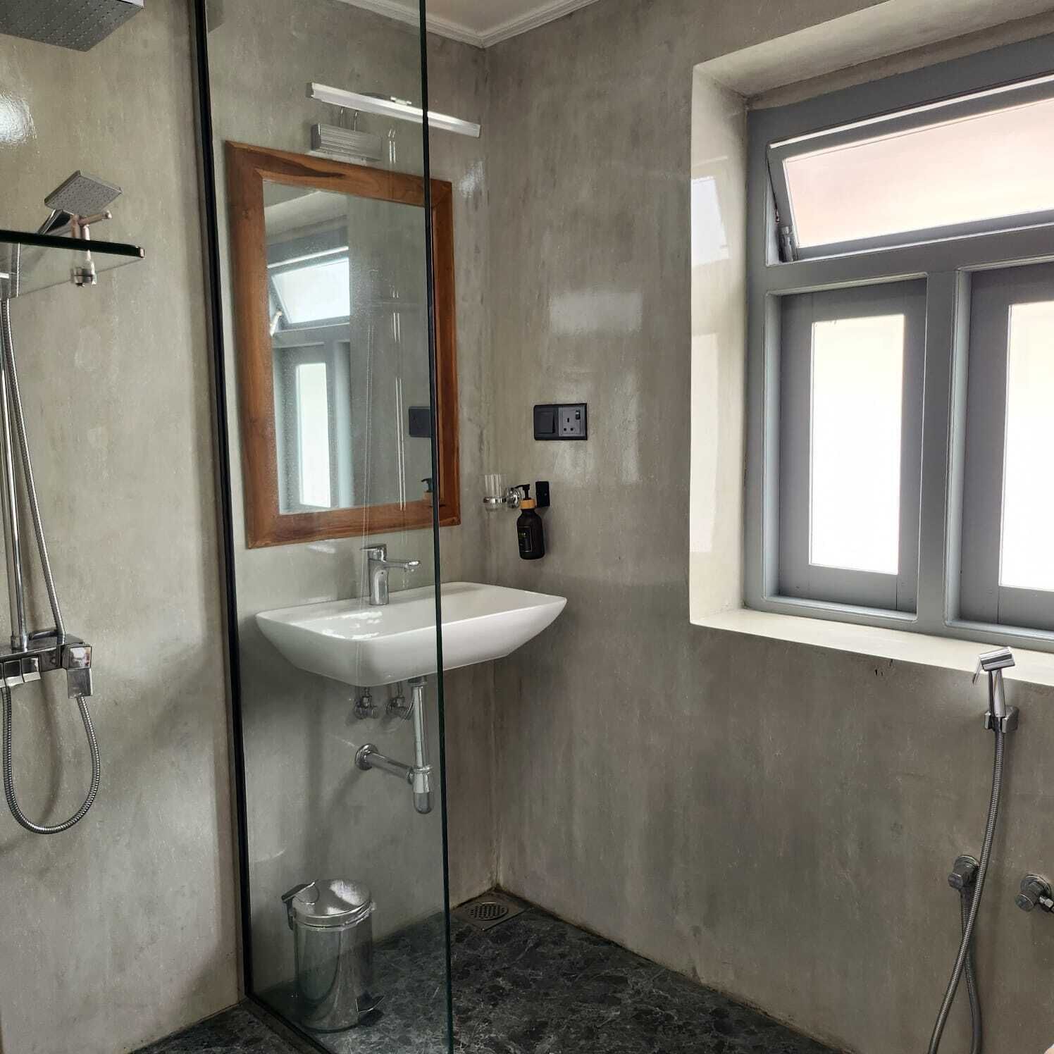 A bathroom with a glass-enclosed shower, a white sink, and a window with a view.