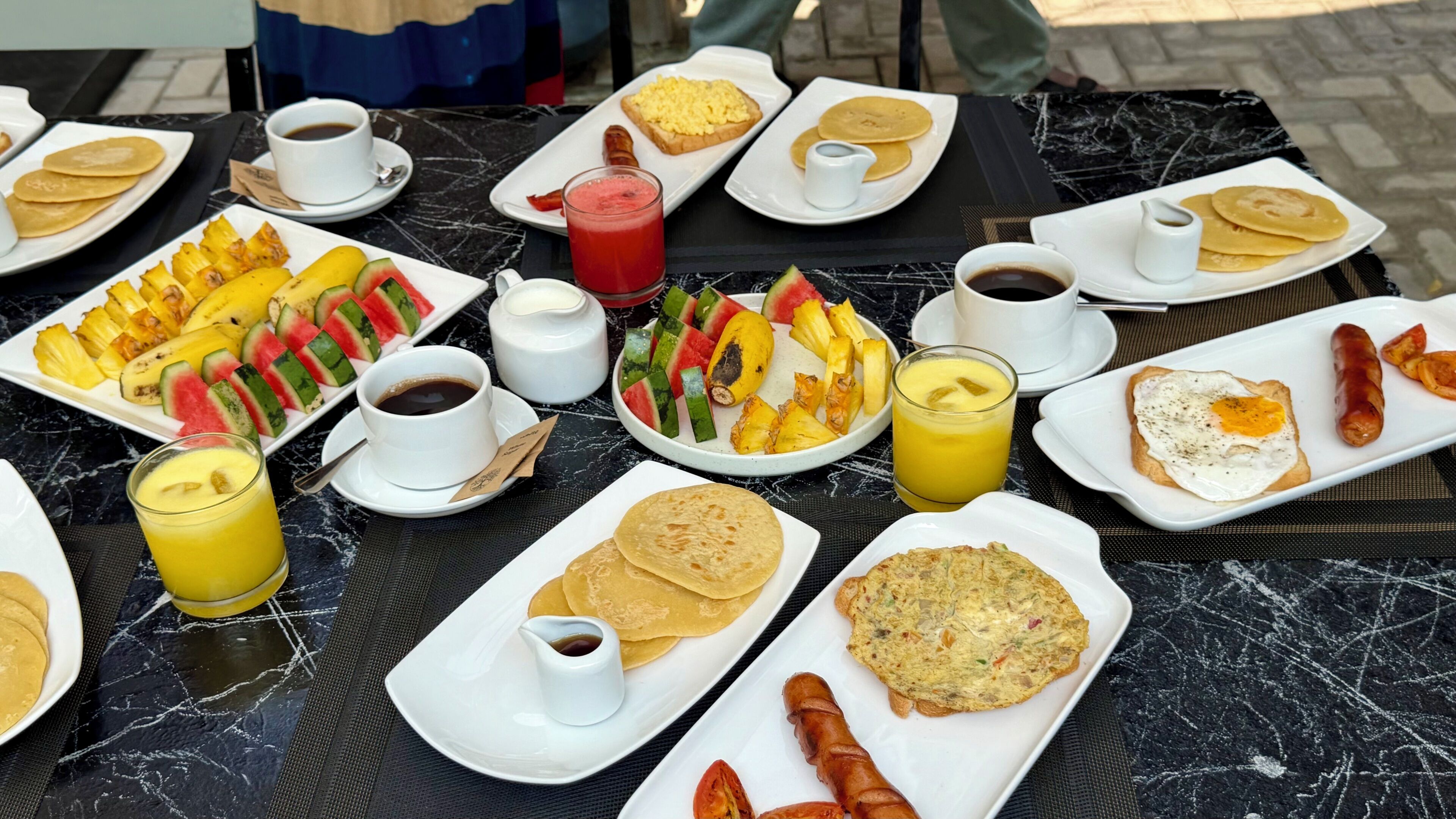 A breakfast buffet with various dishes, drinks, and a marble table.