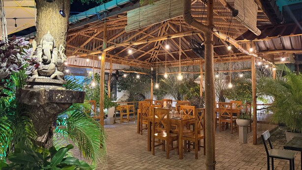 An outdoor restaurant with wooden tables and chairs, a decorative elephant statue, and hanging lights. - Neem Tree House (Trincomalee)