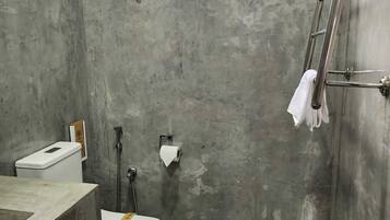 Un baño con pared de concreto, ventana, inodoro, lavamanos y zona de ducha.