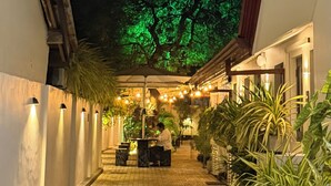 A nighttime corridor with a tree illuminated in green, a tiled floor, and a person working at a counter.