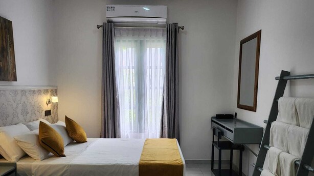A hotel room with two beds, a desk, a chair, a ladder, and a large window with curtains.
