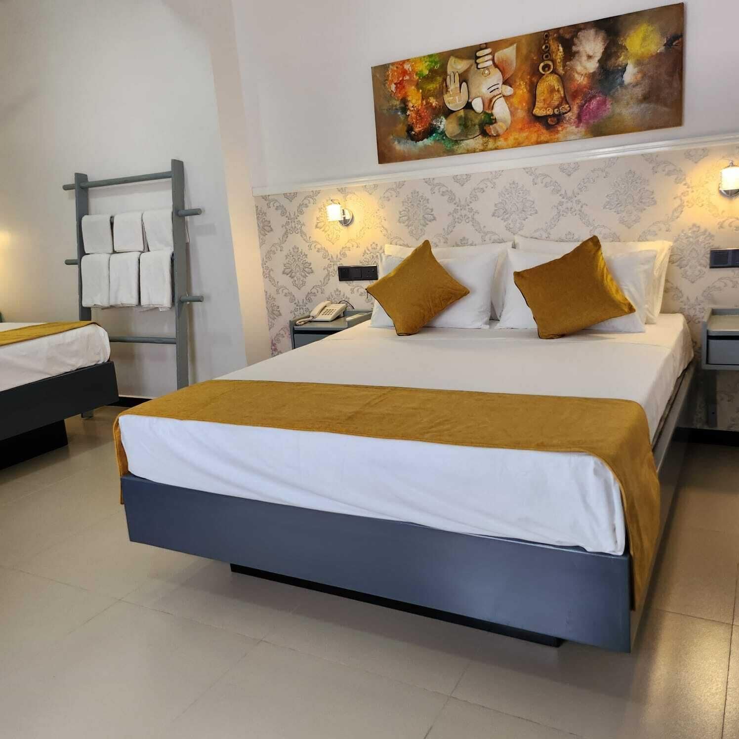 Habitación de hotel con una cama grande, una mesita de noche con lámpara, teléfono e iluminación en la pared.