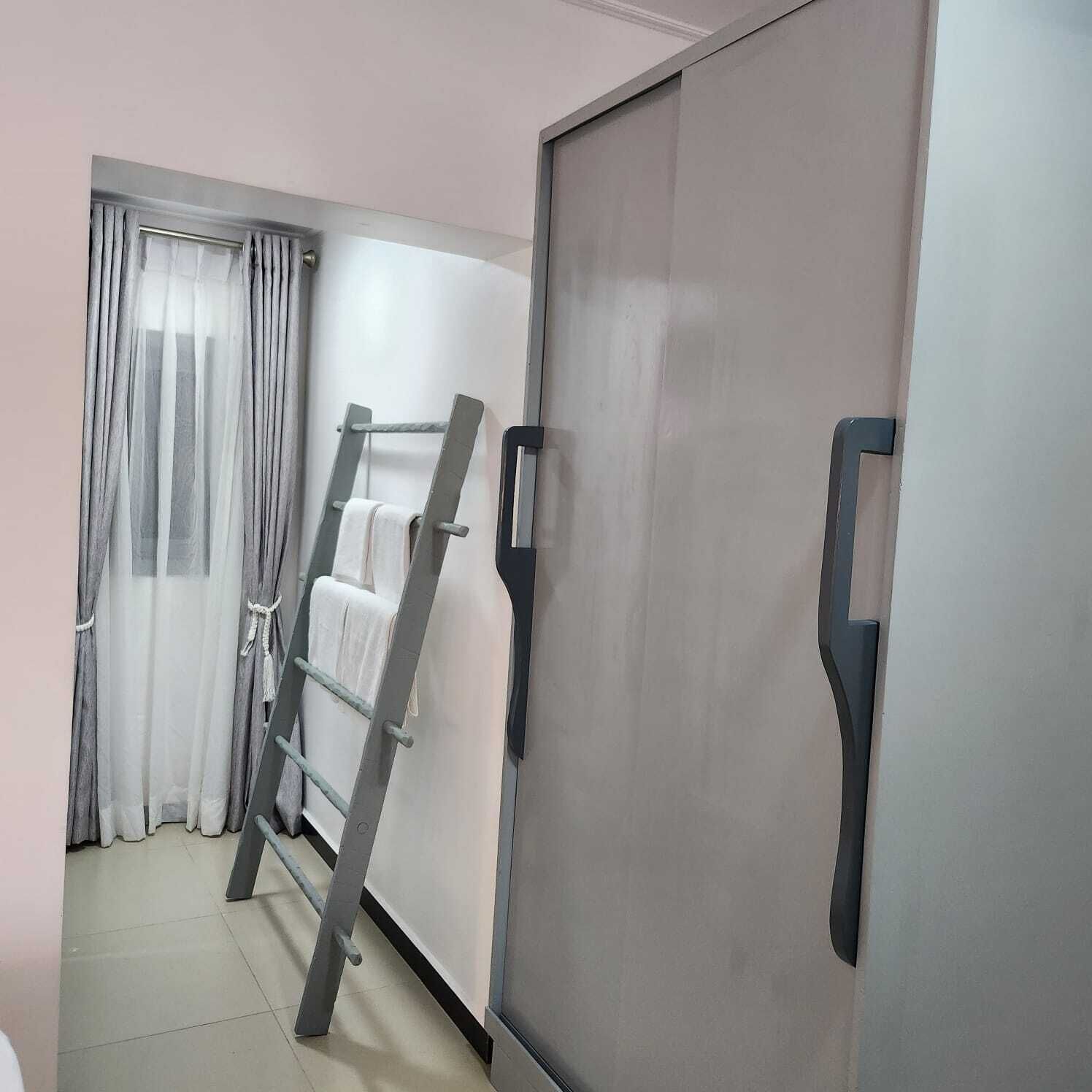 Una habitación con armario, una escalera apoyada en la pared y una ventana con cortinas de gasa.