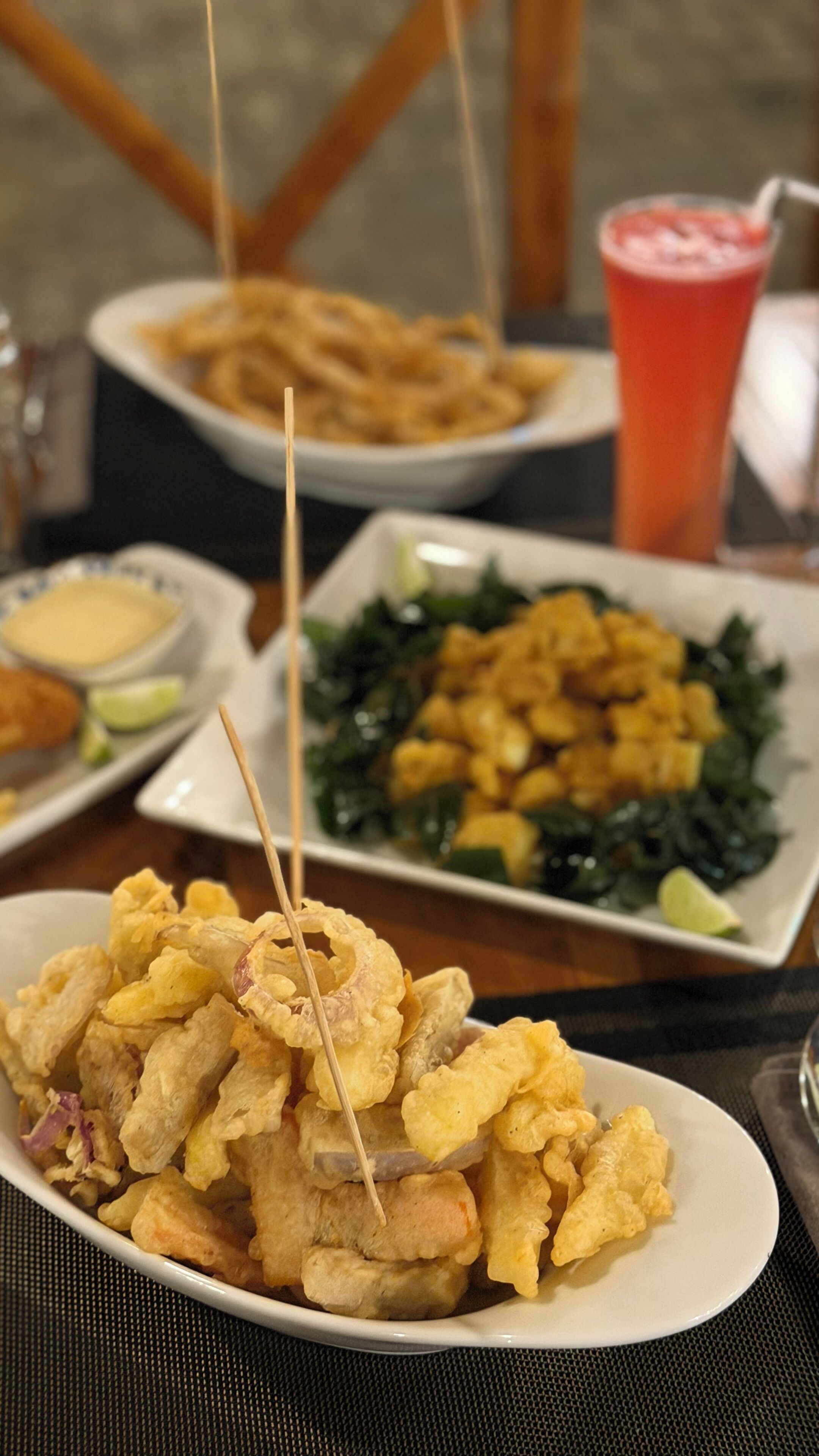 A table with various dishes including fried food, a drink, and a plate of greens.