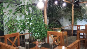 A wooden dining area with tables and chairs, surrounded by greenery and a bamboo ceiling structure. - Neem Tree House (Trincomalee)