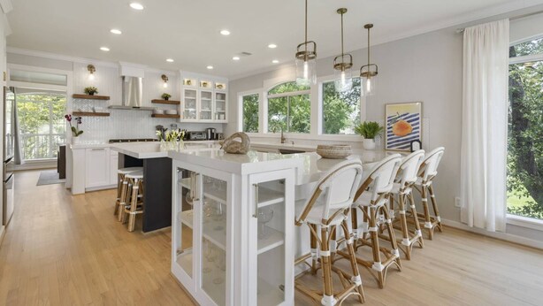Une cuisine moderne avec des meubles blancs, un îlot central doté de portes en verre et un coin repas avec des chaises en osier.