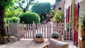 A covered patio area with a wicker chair and a table, a white picket fence, and potted plants. - Clos saint Joseph (Orange)