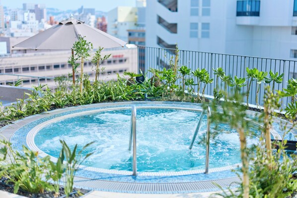 Una piscina en la azotea con hidromasaje, rodeada de plantas, y un paisaje urbano al fondo.
