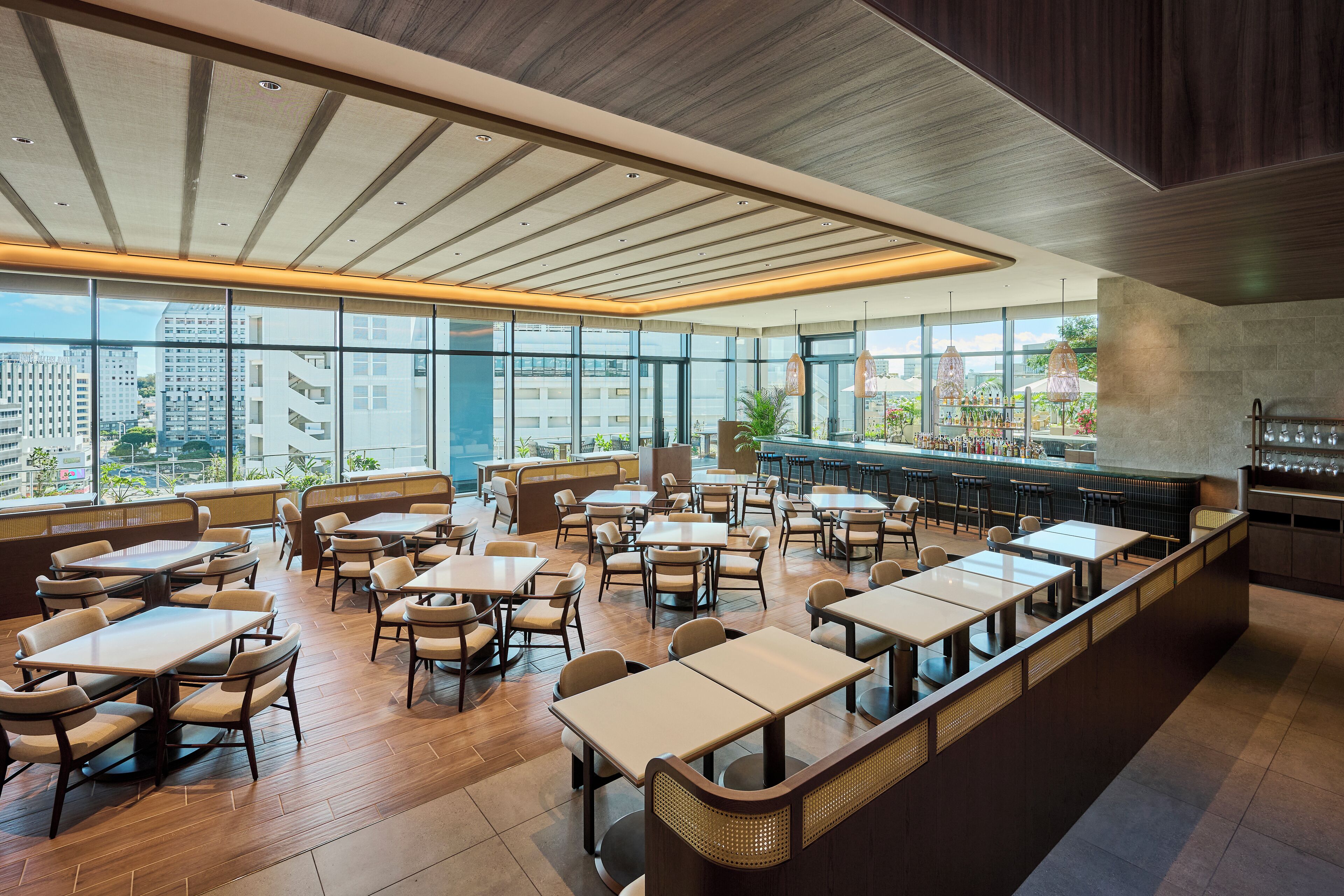 Un restaurante espacioso con techos altos, amplias ventanas que ofrecen vistas a la ciudad y una zona de bar central.