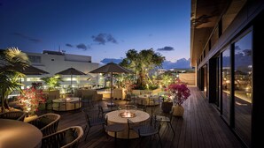 Un espace extérieur aménagé en terrasse, avec des tables et des chaises rondes, des parasols et un foyer.