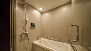 A modern bathroom with a bathtub, shower, and handrails.