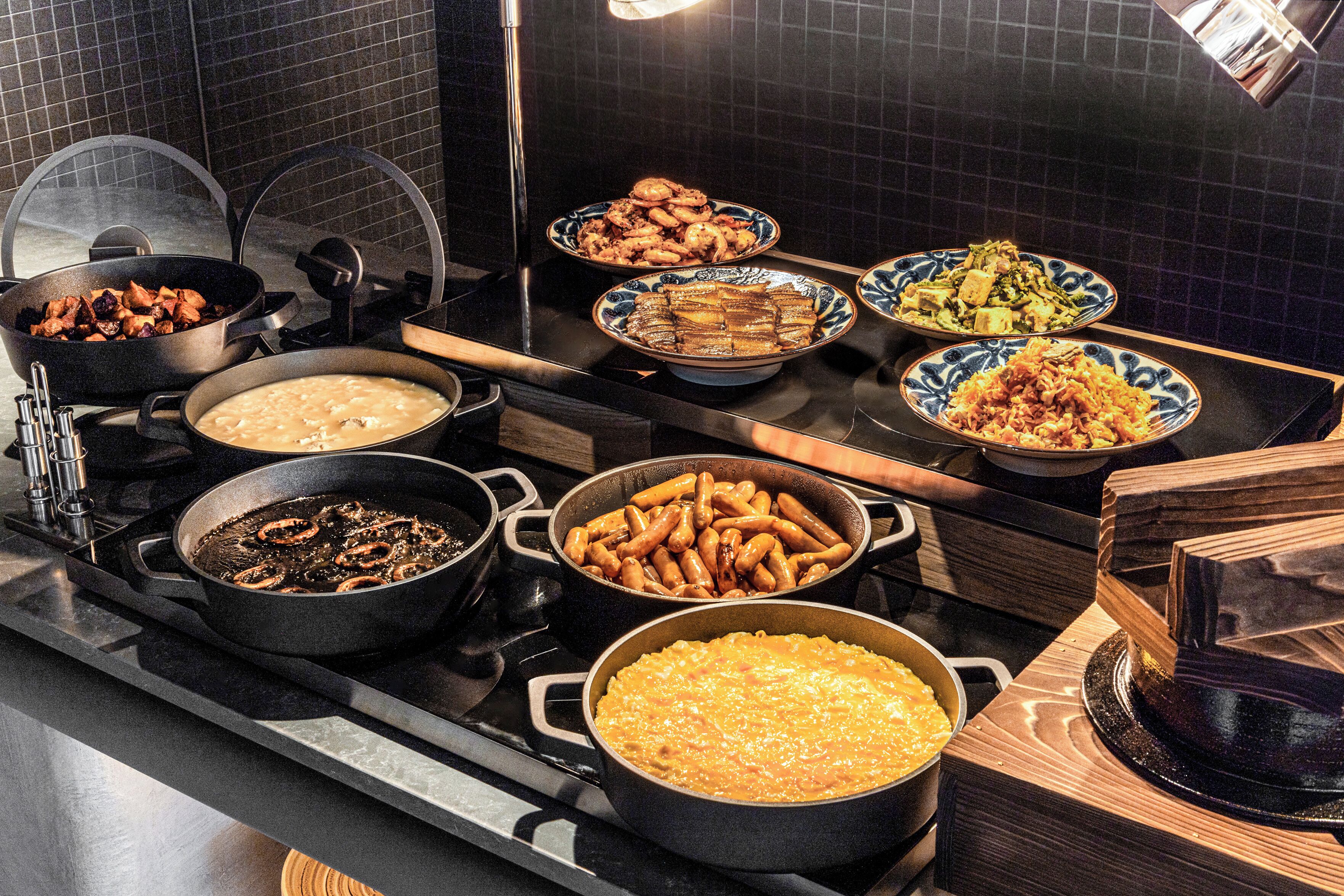 A kitchen with multiple pots and pans on the stove, various dishes on the counter, and a tiled backsplash.