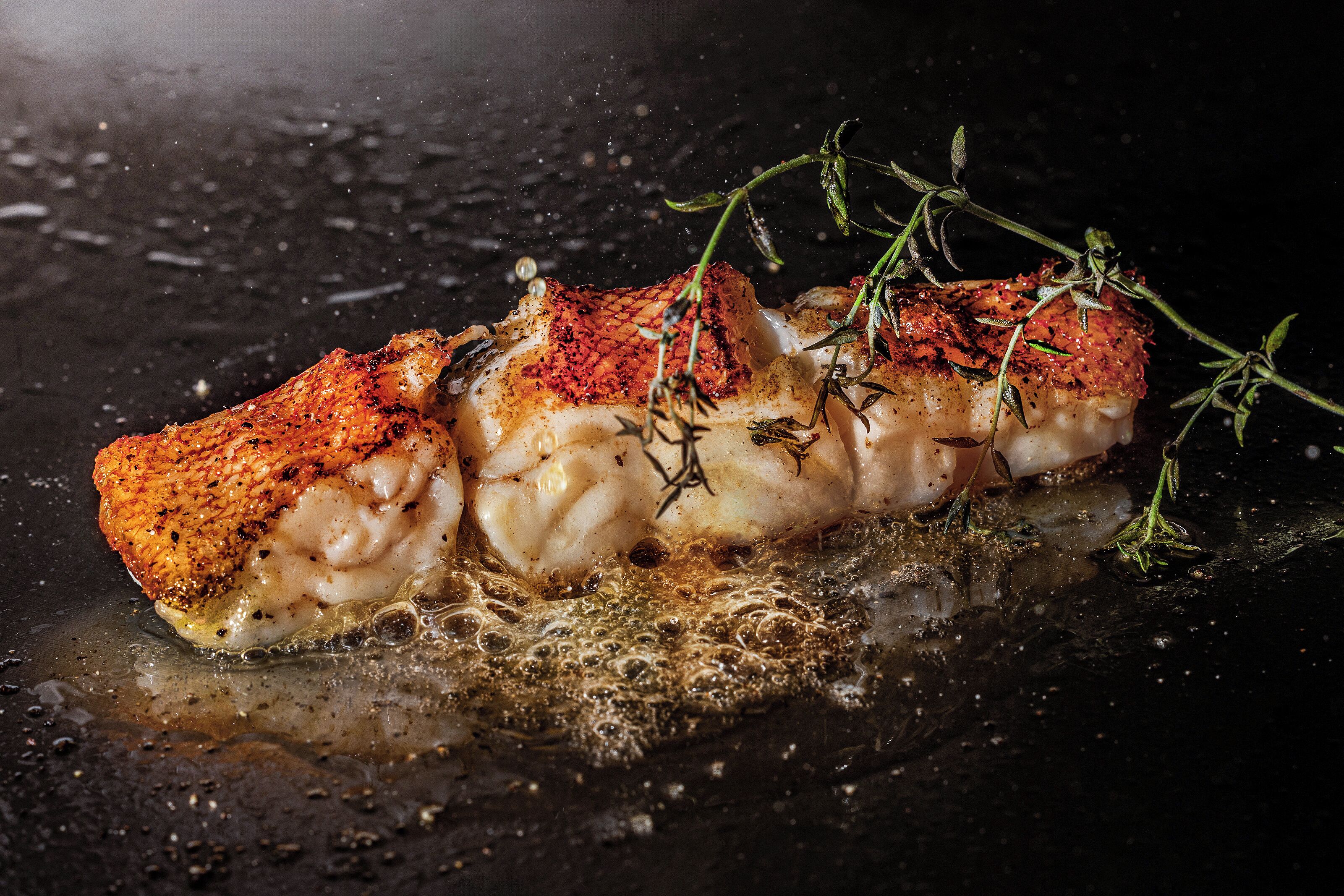 A piece of cooked fish with herbs on a dark surface.