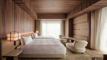 A hotel room with a large bed, a bedside table, a chair, a small round table, and a window with curtains.