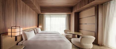 A hotel room with a large bed, a bedside table, a chair, a small round table, and a window with curtains.