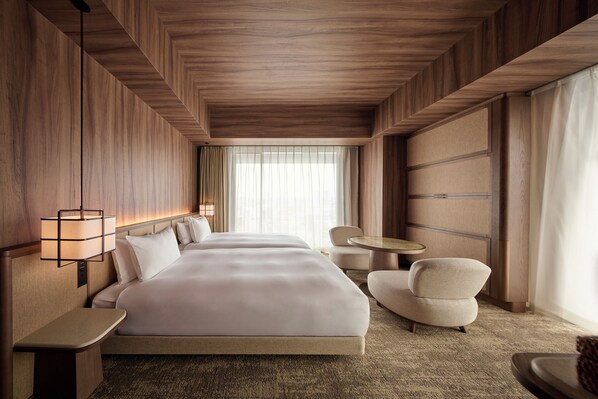 Habitación de hotel con una cama grande, una mesita de noche, una silla, una pequeña mesa redonda y una ventana con cortinas.