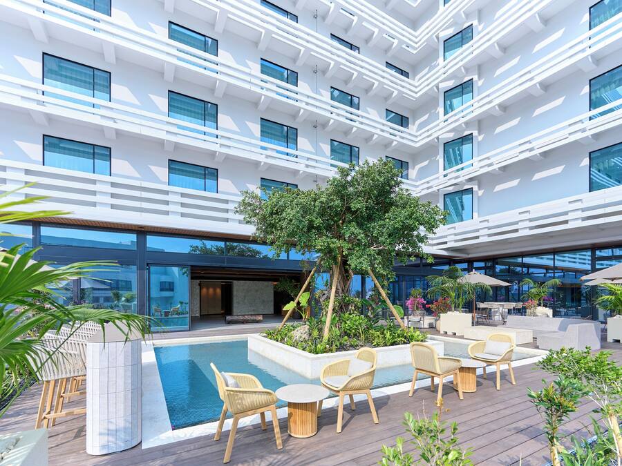 A modern hotel with a rooftop pool area, outdoor seating, and lush greenery.