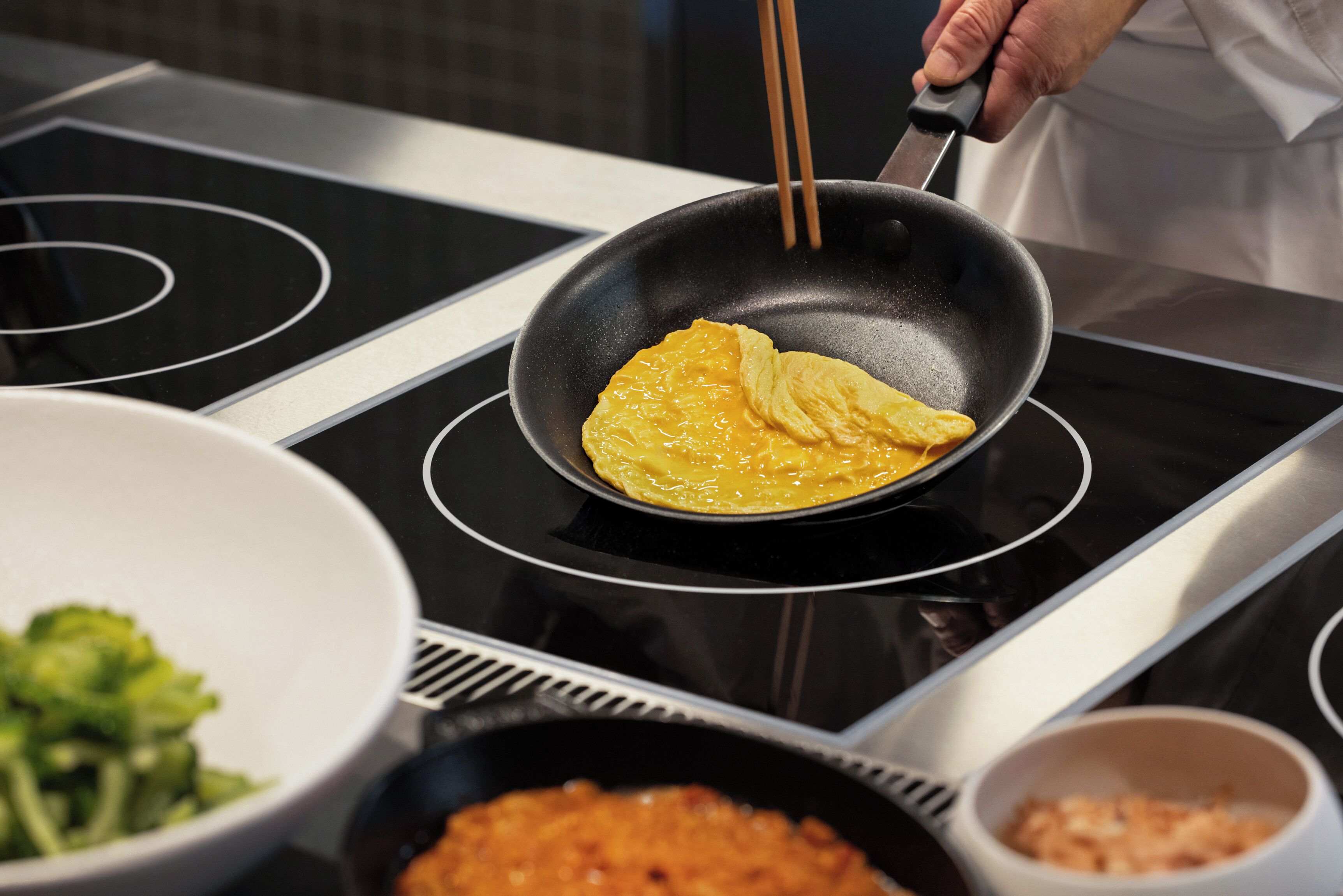 A kitchen with a black stovetop, a pan with food, and bowls of food.