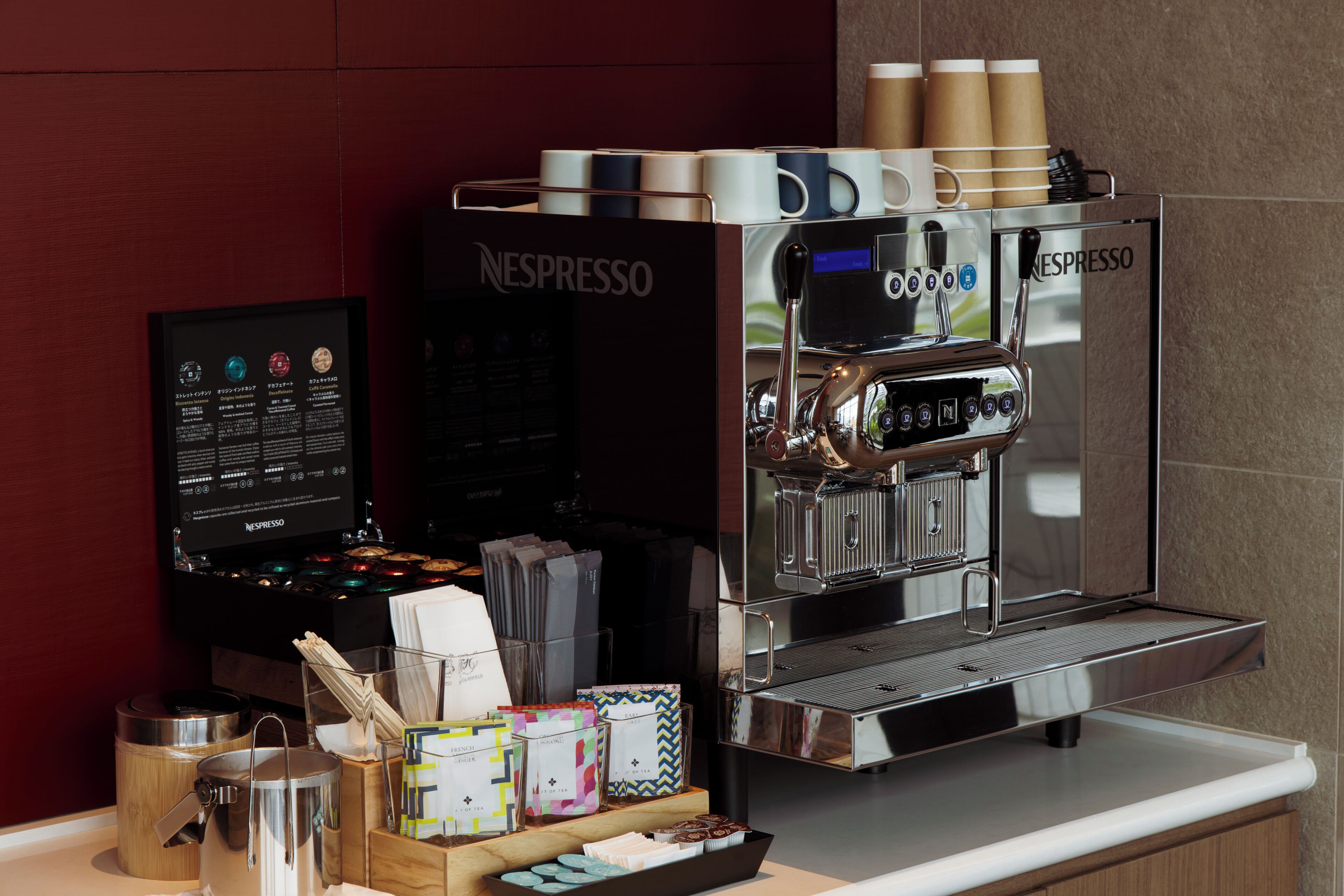 A commercial espresso machine with a digital display, a coffee machine, and various coffee pods and cups on a counter.