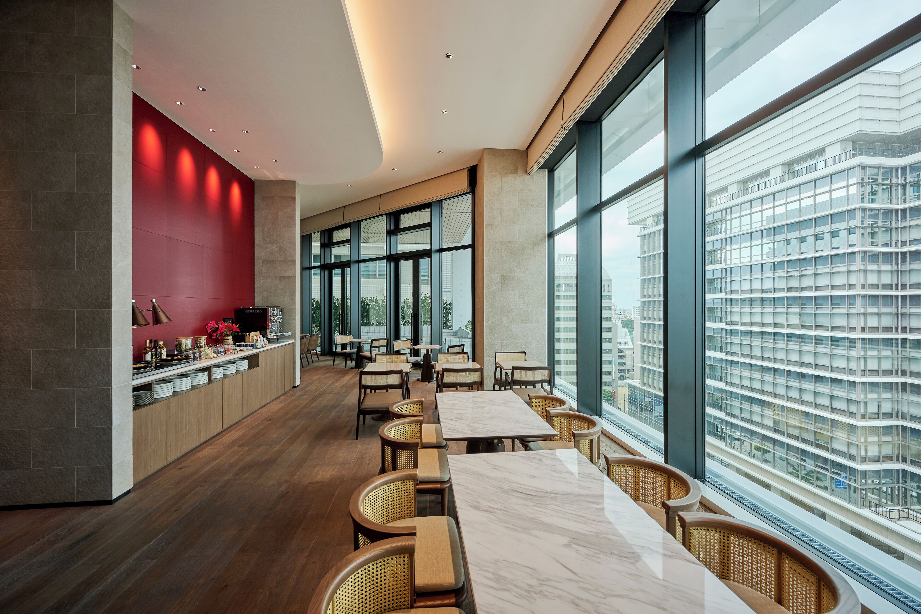 A modern dining area with a long table and chairs, large windows, and a view of a cityscape.