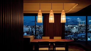 A modern dining area with a city view, featuring a wooden table and chairs, and pendant lighting.