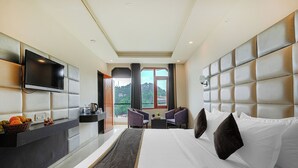 Een moderne hotelkamer met een groot bed, een flatscreen televisie, een bureau met stoel en uitzicht op het groen.