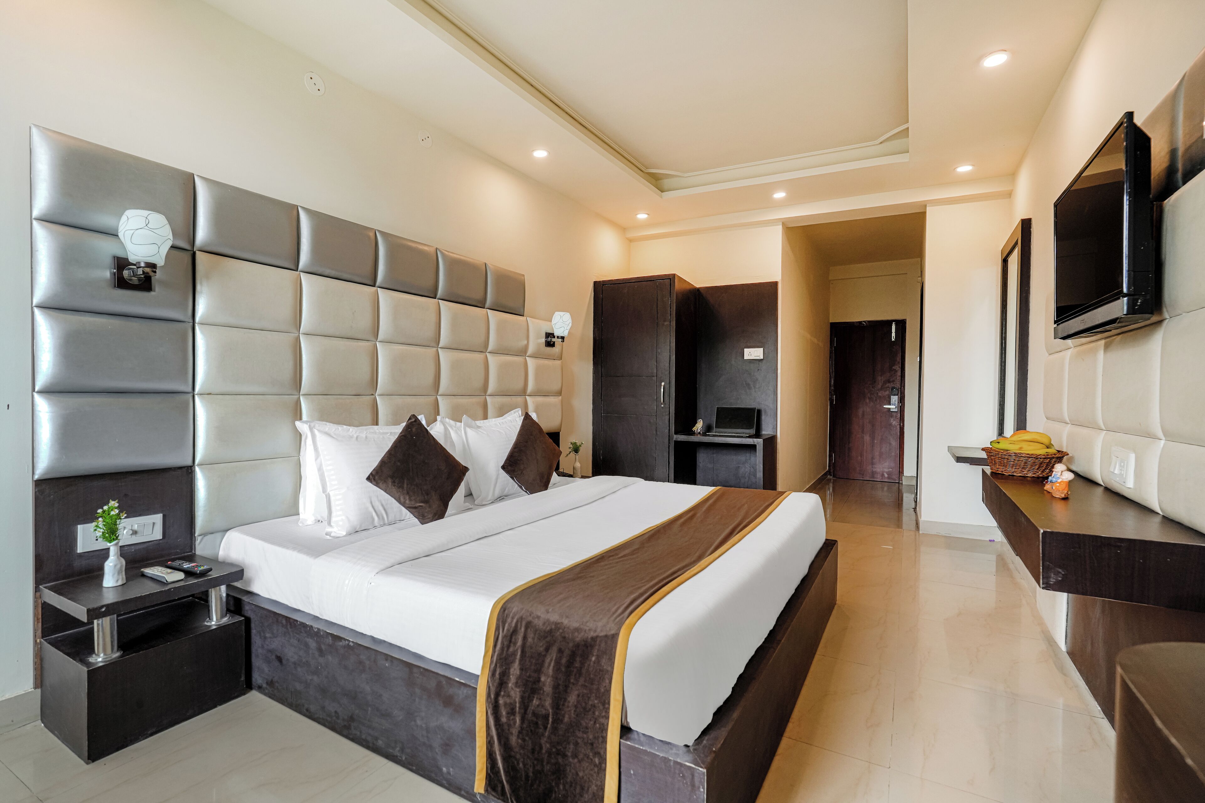 A modern hotel room with a large bed, a bedside table, a TV, and a wardrobe.