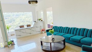 Een moderne woonkamer met een blauwgroene bank, een glazen salontafel en een wand bekleed met marmer.
