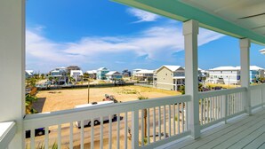 Une propriété située en bord de mer, dotée d’un porche couvert, d’une plage de sable et de plusieurs maisons en arrière-plan.