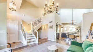 A spacious living area with a staircase, a green sofa, and a chandelier. - Val Vista Lakes Extended Getaway: Hot Tub Access! (Gilbert)