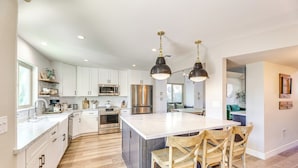 A modern kitchen with white cabinets, stainless steel appliances, and a large island with bar stools. - Val Vista Lakes Extended Getaway: Hot Tub Access! (Gilbert)